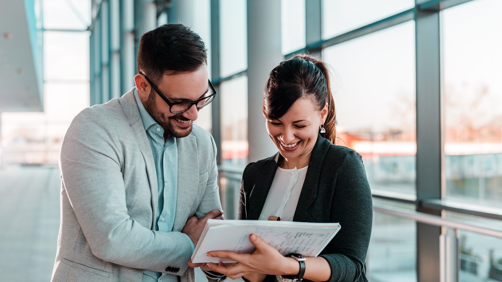 A RegLeg partner and a regulated-industry buyer shaking hands in a boardroom, a wall-mounted TV presenting the RegLeg compliance editions, solid navy wall, navy and teal lighting.